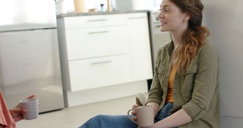 Cozy kitchen conversation with friends sitting on floor holding ribbed mugs in daylight