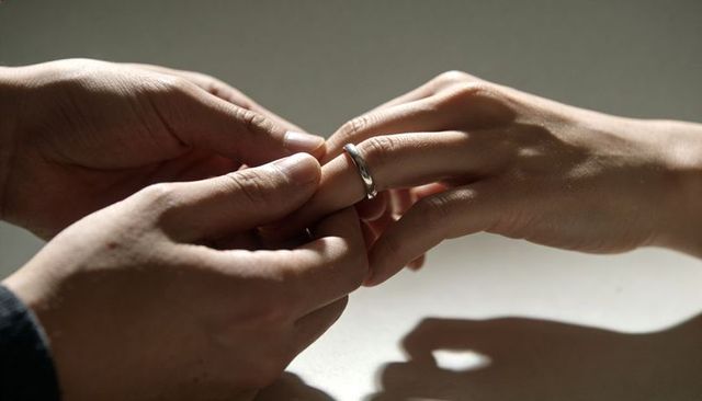 Intimate close-up of two hands placing plain silver wedding ring on finger