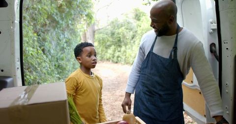 Small business vendor loading fresh produce from cargo van while talking with young helper