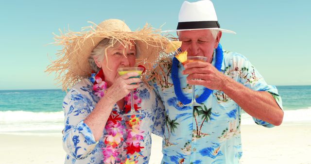 Senior couple standing on tropical beach, both wearing colorful flower leis and straw hats. They are holding and sipping on cocktails while smiling. Ideal for use in travel advertisements, retirement planning promotions, lifestyle magazines, and summer vacation marketing materials.