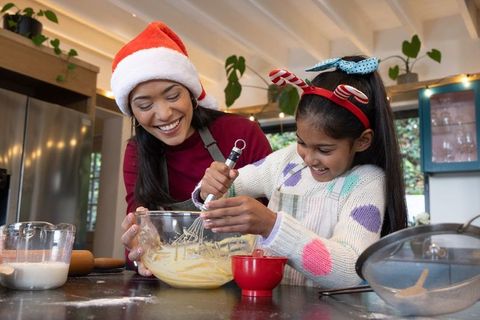 Asian mother and daughter whisking holiday batter wearing santa hat and reindeer headband
