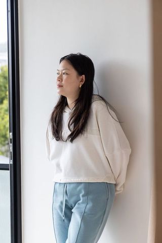 Asian woman leaning by window in cozy loungewear, serene natural light and balcony view