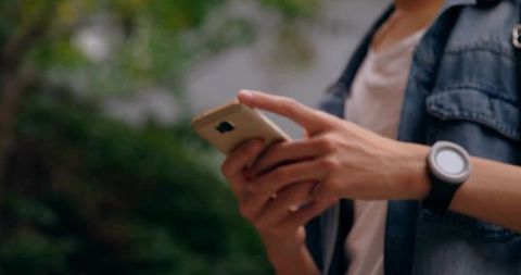 Young man scrolling smartphone while wearing smartwatch in denim jacket outdoors