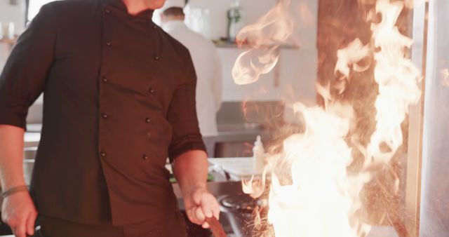 Caucasian male chef frying food in frying pan with bursting fire in kitchen, slow motion. Cooking, profession, food, restaurant and catering, unaltered.