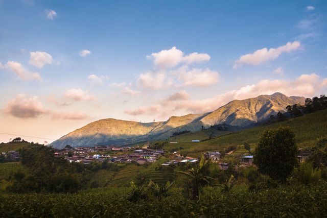 The image captures a picturesque mountain village bathed in the warm glow of sunset. Nestled among lush green fields and cradled by rolling hills, the scene exudes tranquility and peace. Ideal for travel blogs, marketing materials highlighting rural tourism, backgrounds for inspirational content, or any project emphasizing serenity and the beauty of nature.