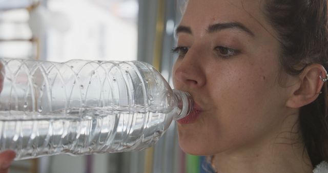 Biracial woman drinking water from bottle in gym. Fitness, sport, healty lifstyle and food and drink, unaltered.