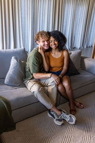 Young couple cuddling on sofa showing bracelet, cozy modern living room intimacy