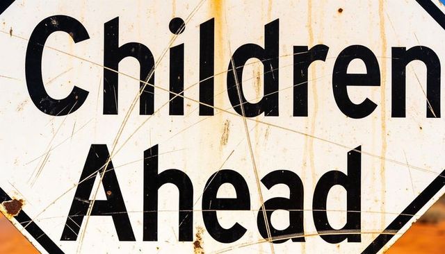 Weathered children ahead sign closeup showing rusty scratches and worn black text