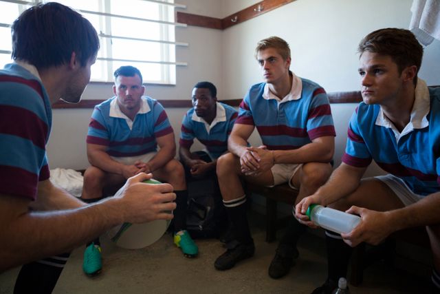 Rugby team disscusiing while sitting on bench in locker room