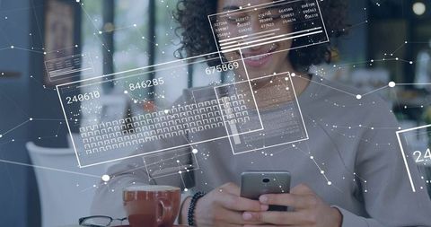 Curly woman using smartphone with AR data overlays in modern coworking cafe