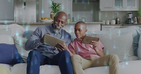 Multigenerational tech mentoring: older man guiding teen using tablets in living room