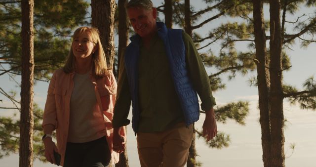 Happy senior caucasian couple holding hands walking in sunny forest, copy space. Relationship, retirement, wellbeing and active senior lifestyle, unaltered.