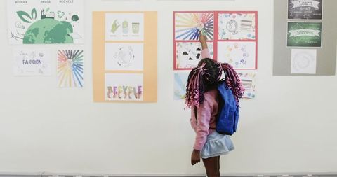 Curious Child with Backpack Pointing at Bright Classroom Posters