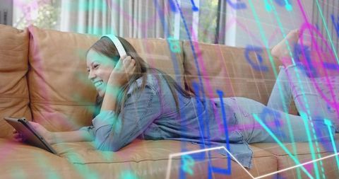 Teen female wearing headphones using tablet on sofa with neon augmented reality overlays