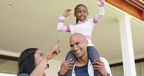African american family laughing and playing on porch, dad carrying daughter on shoulders