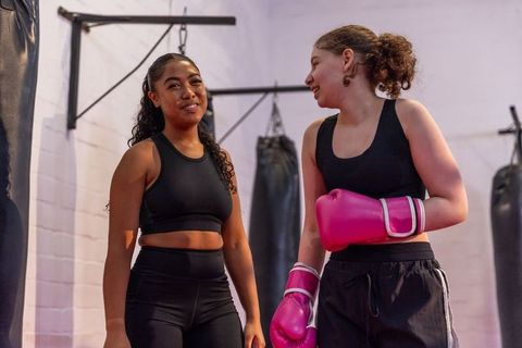 Female trainer coaching teen boxer wearing pink gloves, smiling and chatting in gym