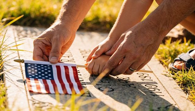 Placing american flag on veteran headstone with child and parent hands, memorial tribute