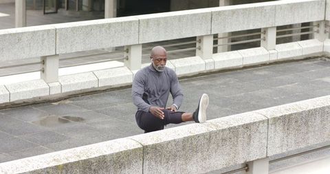 Mature african american man stretching hamstring on urban concrete railing during workout