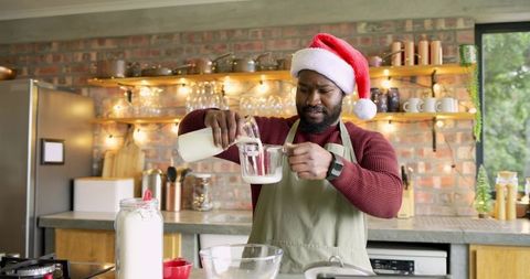 African American man wearing Santa hat pouring milk for holiday baking in rustic kitchen