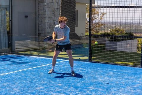 Male athlete preparing to hit padel ball on sunlit blue private court