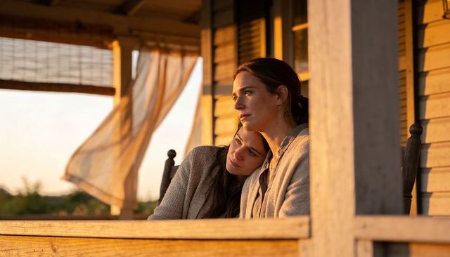 Two women leaning on wooden porch at sunset embracing quiet golden-hour companionship