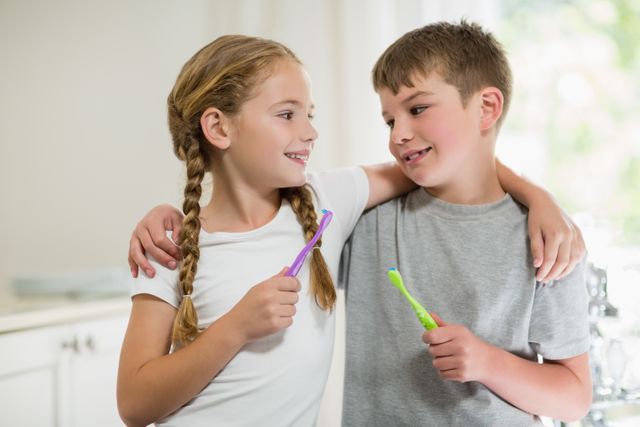 Smiling siblings brushing teeth in bathroom at home