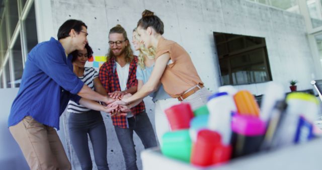 Diverse group of colleagues collaborating and putting their hands together in the office. Can be used to represent teamwork, diversity, team spirit, office environment, corporate culture, unity, and effective collaboration in workplace.