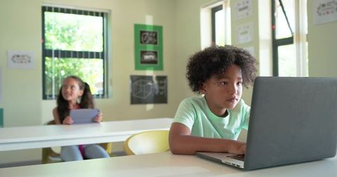 African American students using laptop and tablet in bright classroom using technology