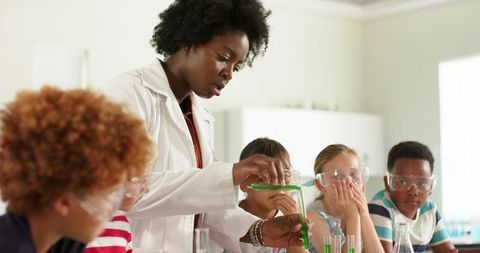 African American teacher demonstrating chemistry experiment to curious students in goggles