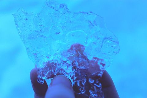 Hand holding crystal clear ice shard under arctic blue light close-up