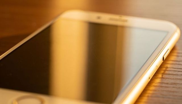 Closeup smartphone reflecting warm vertical light on wooden table with smudged screen and home butto
