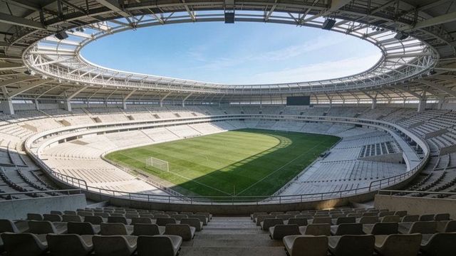 Empty modern football stadium showing pristine turf, curved seating bowl and open oval roof