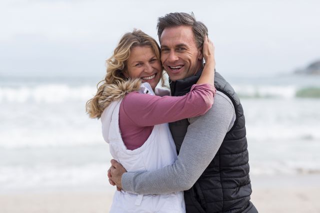 A heartwarming moment featuring a mature couple smiling and hugging on a beach. Perfect for use in lifestyle, tourism, and relationship-themed marketing materials, advertisements, and websites highlighting middle-aged romance or vacation promotions.
