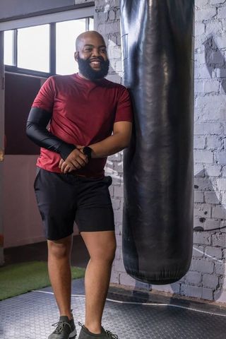 African american man leaning beside punching bag smiling wearing smartwatch and training