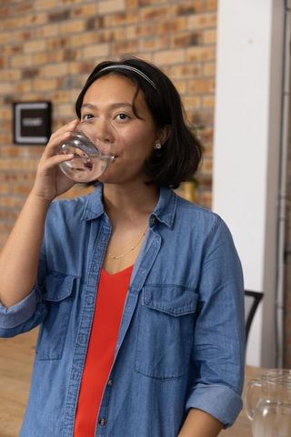 Asian Woman in Denim Shirt Enjoying Refreshment at Rustic Cafe