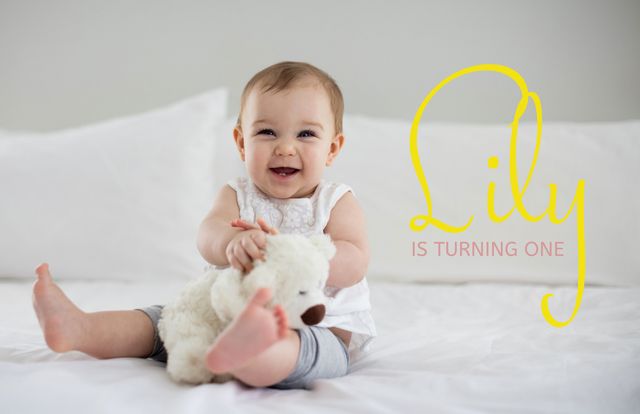 Capturing the essence of a first birthday celebration, this cheerful baby cuddles a plush toy on a white bed. Ideal for birthday invitations, parenting blogs, and nursery decor.