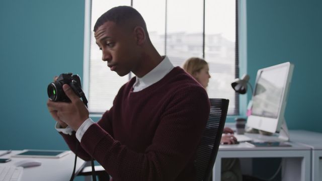 Creative professional adjusting camera in a modern office while a female colleague works in the background. Perfect for themes of teamwork, creativity, technology, and office environments. Suitable for business articles, tech blogs, or creative industry insights.