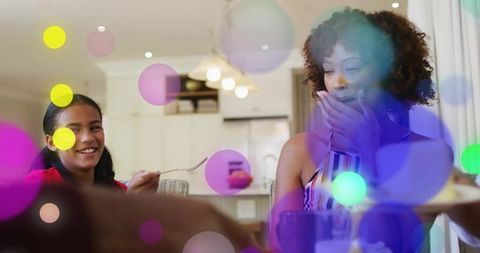 Woman reacting with surprise at kitchen table as child offers spoon during mealtime
