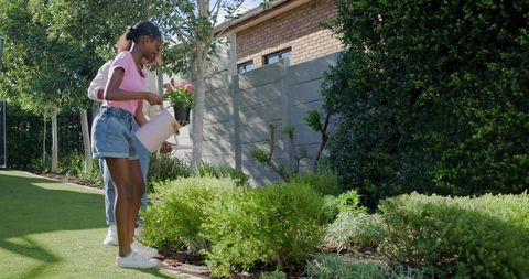 Mother and daughter watering plants together in sunny suburban backyard garden
