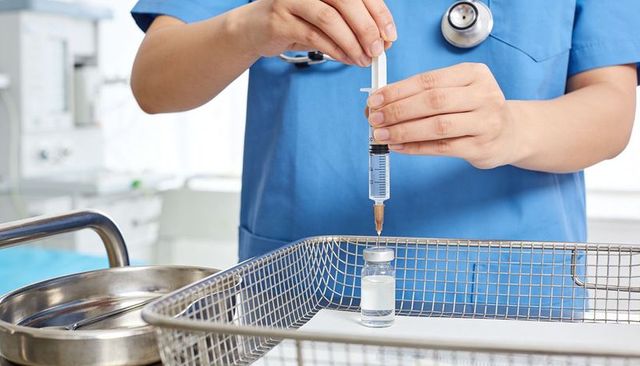 Nurse in blue scrubs drawing medication into syringe from vial on sterile tray in hospital
