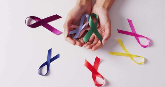 Hands of caucasian woman and multi coloured ribbons on white background. Medicine, healthcare and health awareness concept.