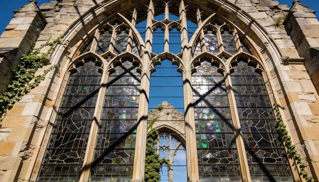 Framing gothic lancet window revealing stained glass and ivy-covered church ruins