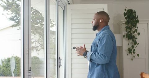 African American man listening with earbuds holding smartphone by sliding glass doors