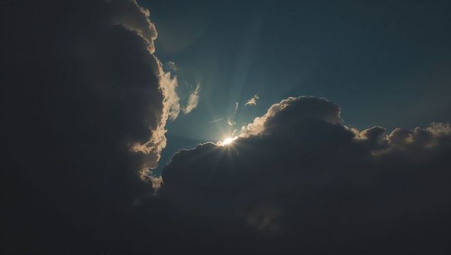 Dramatic Sun Peeking Through Dark Cumulus Clouds Against Blue Sky