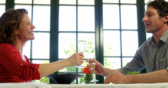 Middle-aged couple enjoying a romantic date at a restaurant, clinking champagne glasses and smiling joyfully. Ideal for depicting romance, special occasions, restaurant ambience, and celebration moments.