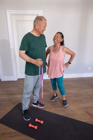Senior chinese couple exercising at home measuring fitness progress with tape and weights