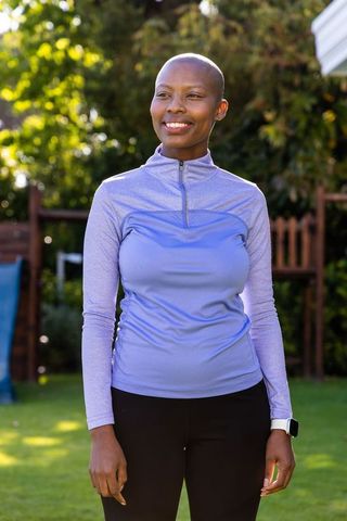 Smiling african american woman in sunny backyard wearing athletic top and smartwatch