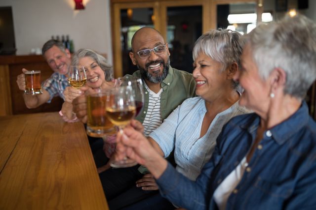 Group of happy friends enjoying drinks together at a bar. They are smiling and raising their glasses in a toast, showcasing a moment of celebration and togetherness. This image is perfect for illustrating social gatherings, friendship, and leisure activities. It can be used in advertisements for bars, restaurants, social events, or articles about the importance of social connections and enjoying life.