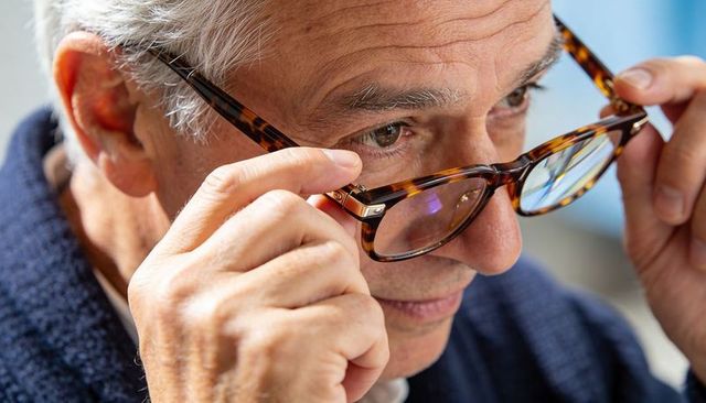 Senior man adjusting tortoiseshell eyeglasses close-up showing wrinkles and focusing gaze