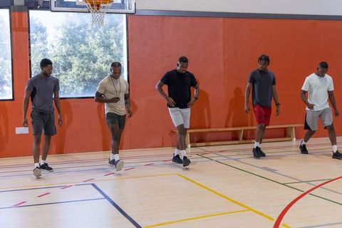 Five african american men practicing basketball footwork drill on hardwood indoor gym court